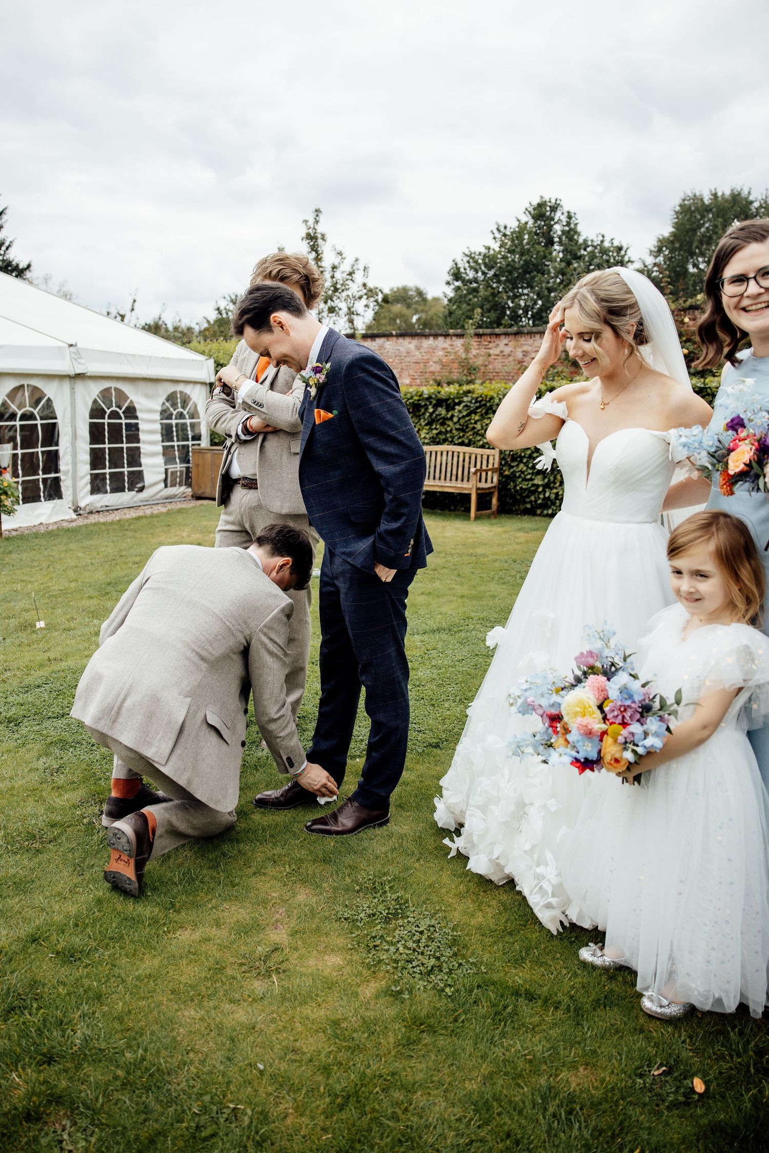 Playful wedding party interactions on grassy lawn during outdoor celebration.