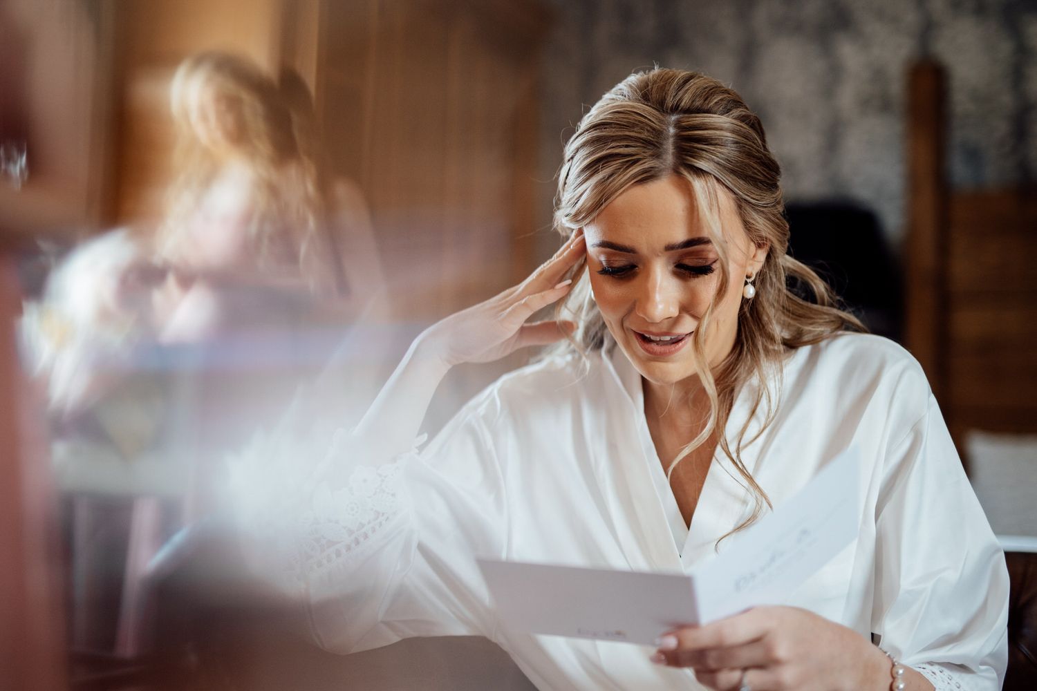 A bride gets ready in the morning light while sitting at a wooden table.