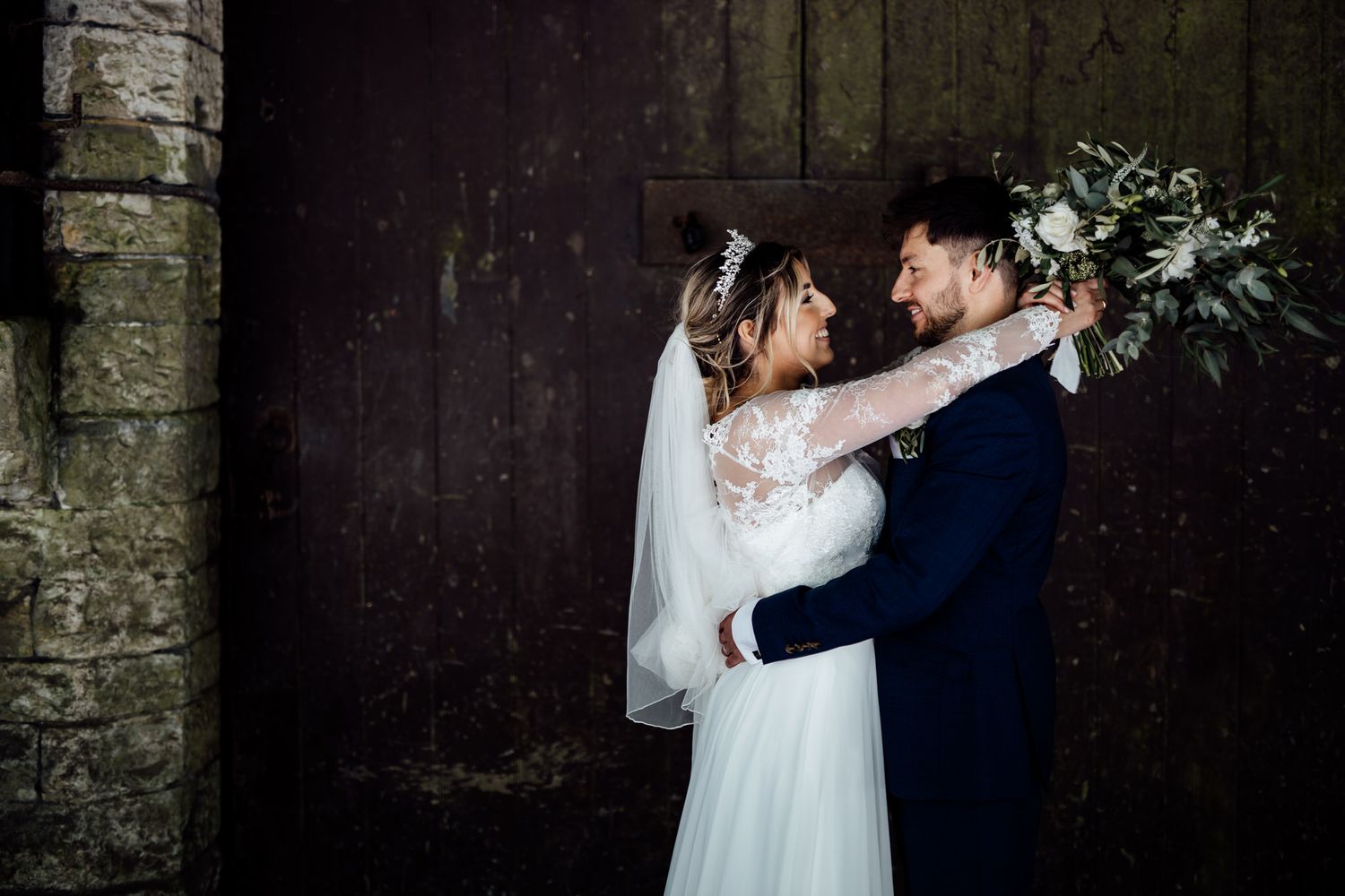 Intimate wedding portrait against dark stone wall with dramatic lighting.