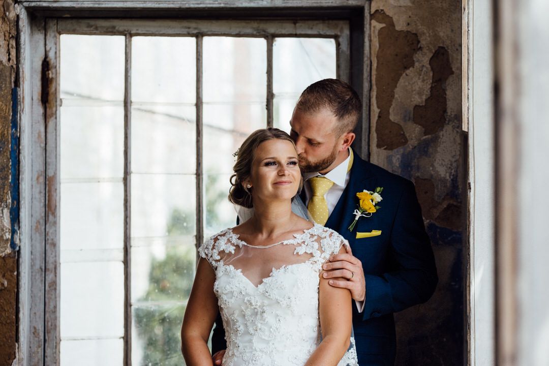 Wedding couple posing in front of large industrial windows in historic building.