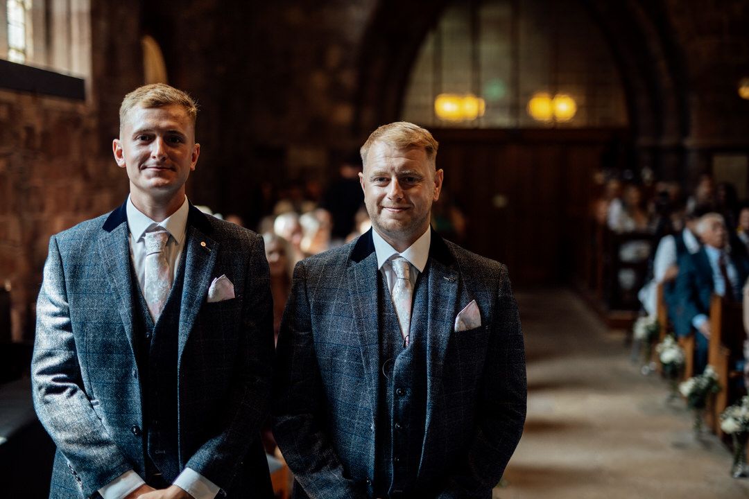 Groomsmen in matching blue suits stand together at a rustic venue.