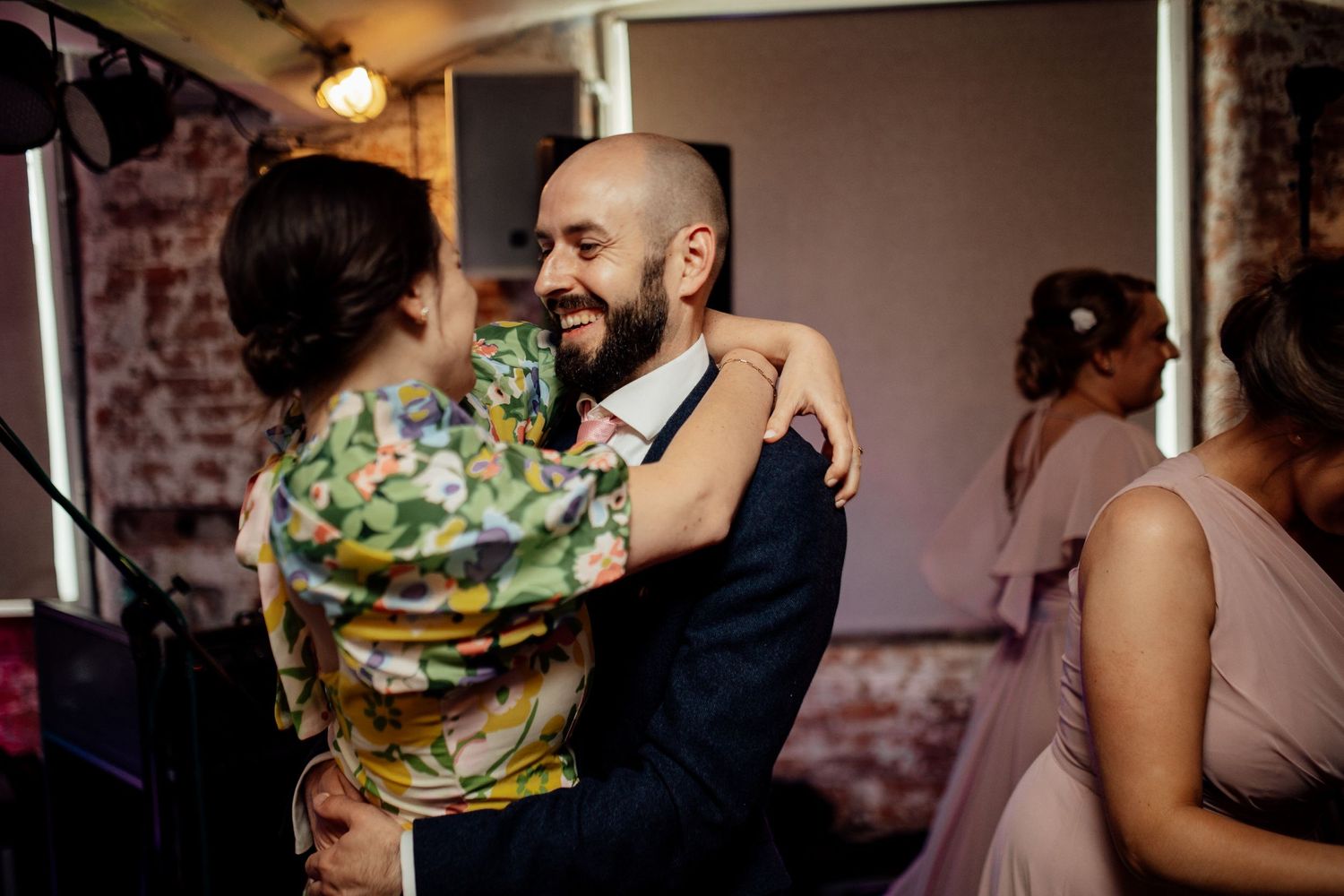 Wedding guests embracing and dancing during an evening reception celebration.