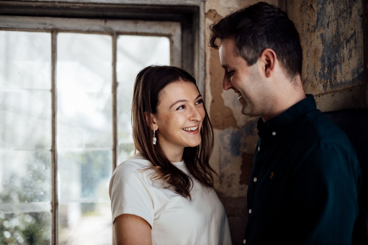 A couple shares tender moments by a window in a weathered industrial building.