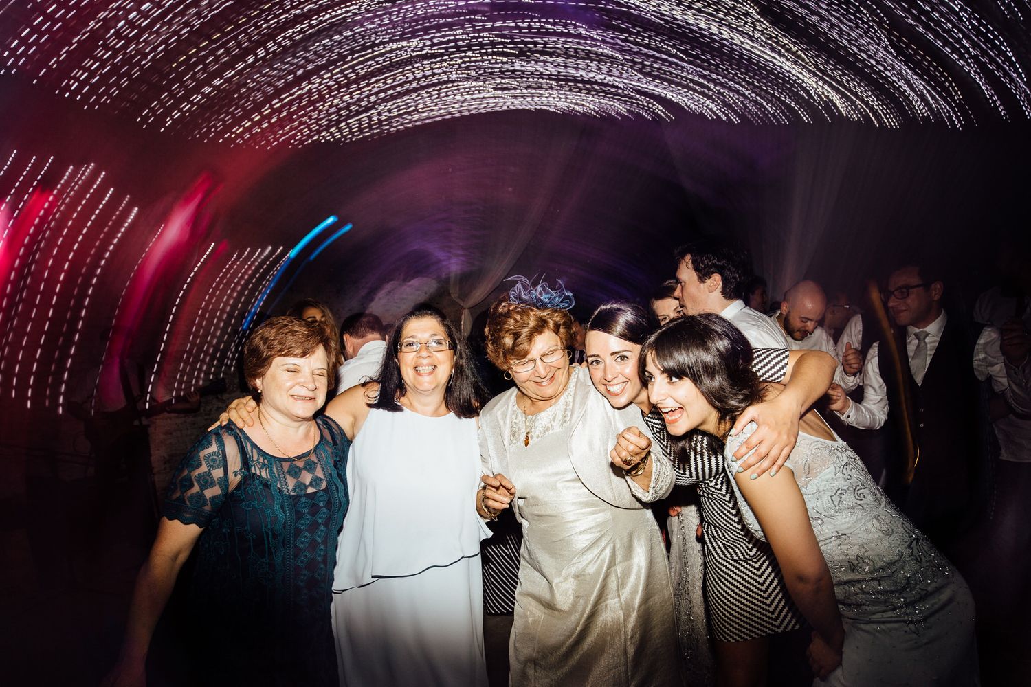 Guests enjoying themselves on a dimly lit dance floor with colorful ambient lighting.