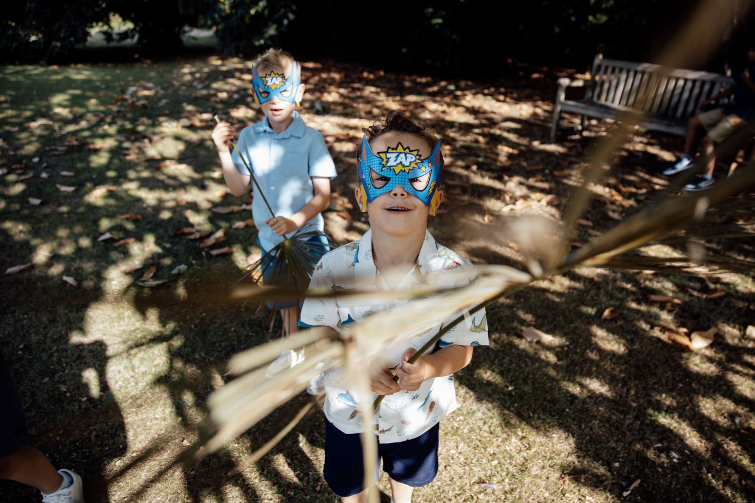 Children playing with toys in dappled sunlight under trees.