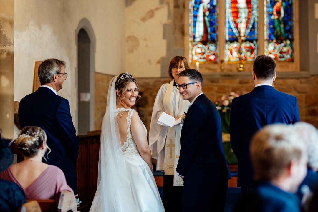 Wedding guests watching ceremony in historic church with colorful stained glass windows.