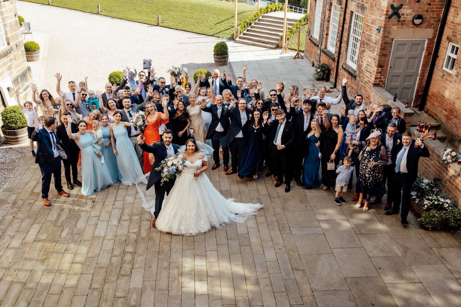 Large wedding group photo with guests on stone courtyard.
