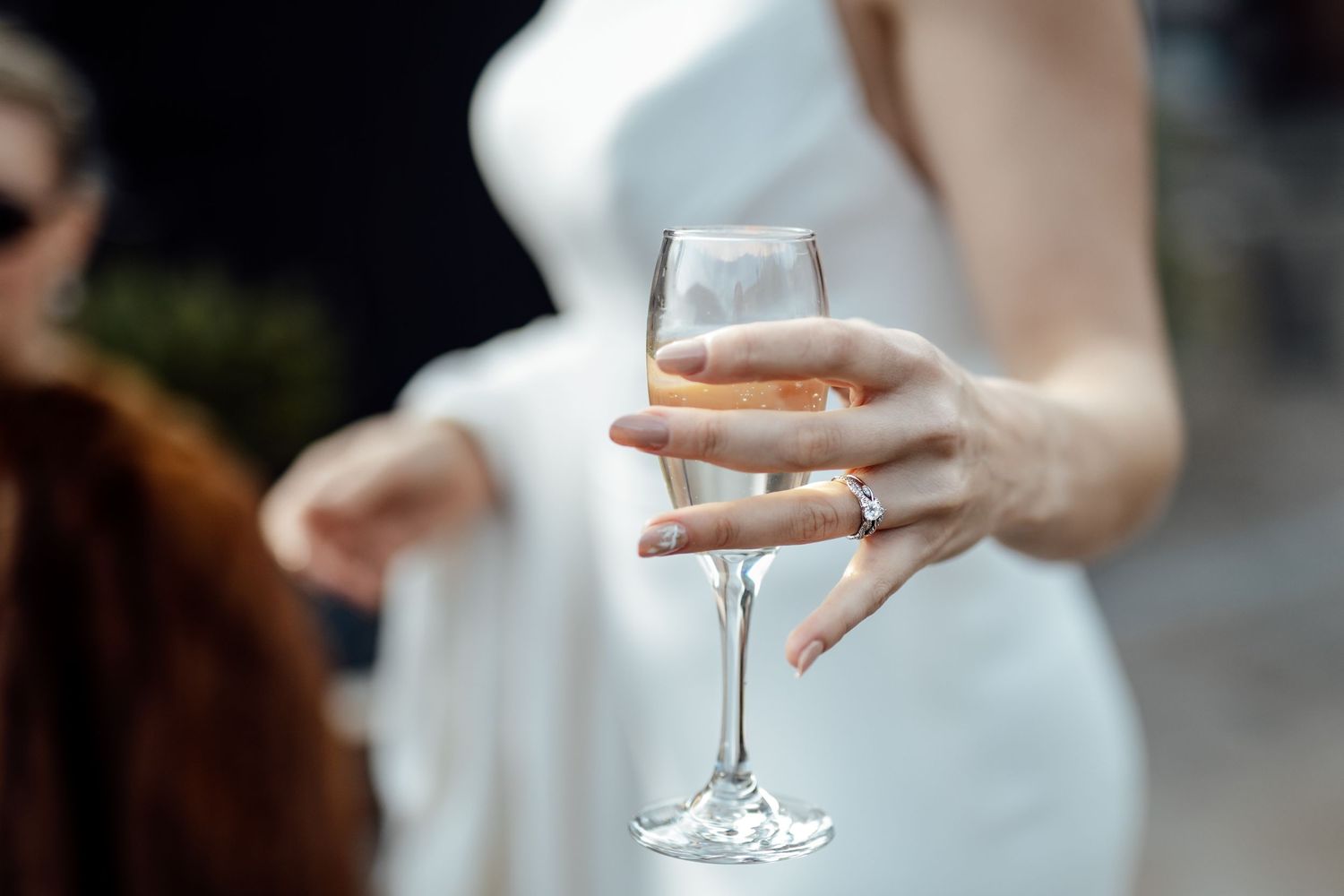 Close-up of wedding ring detail shot with wine glass in background.