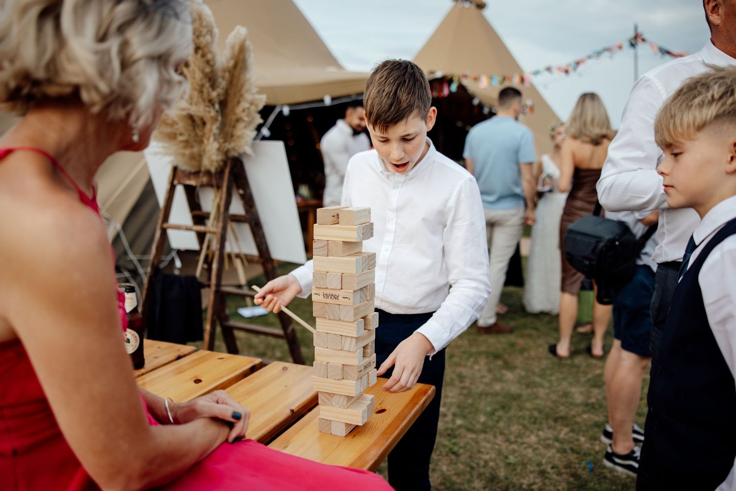 Wedding guests play giant Jenga at an outdoor reception venue.