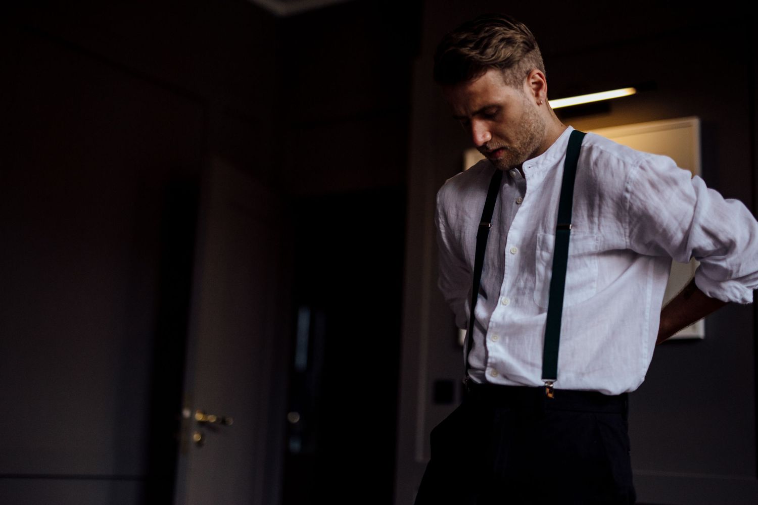 Person adjusting clothing in a dark moody interior setting.