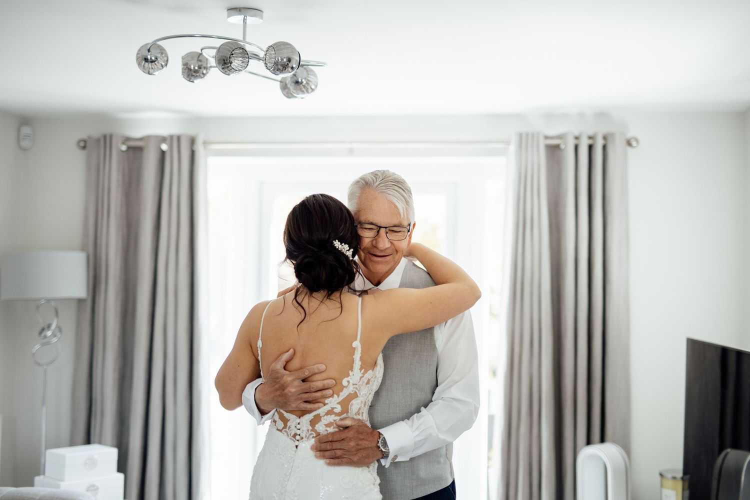 Intimate moment captured in bright, modern room with white curtains and natural light.
