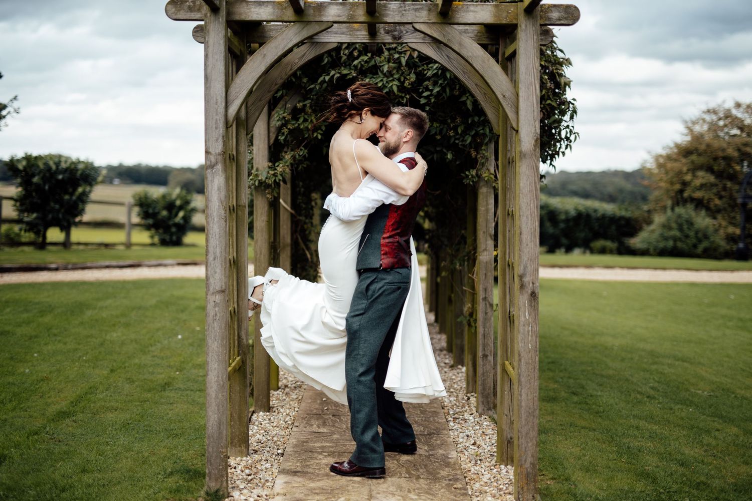 Wedding couple embracing under a stone archway in a scenic outdoor garden setting.
