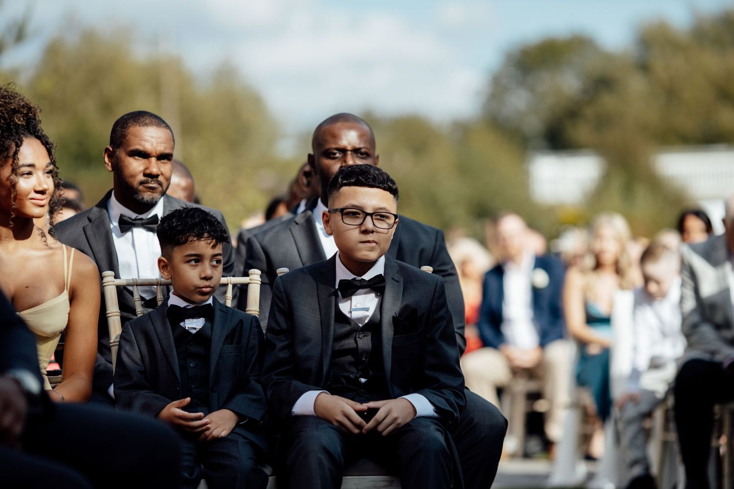 Wedding guests seated in formal attire at outdoor ceremony.