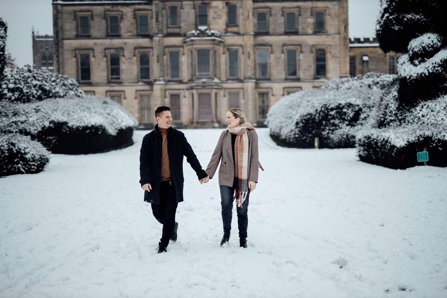 Couple walking in front of historic building surrounded by snow.