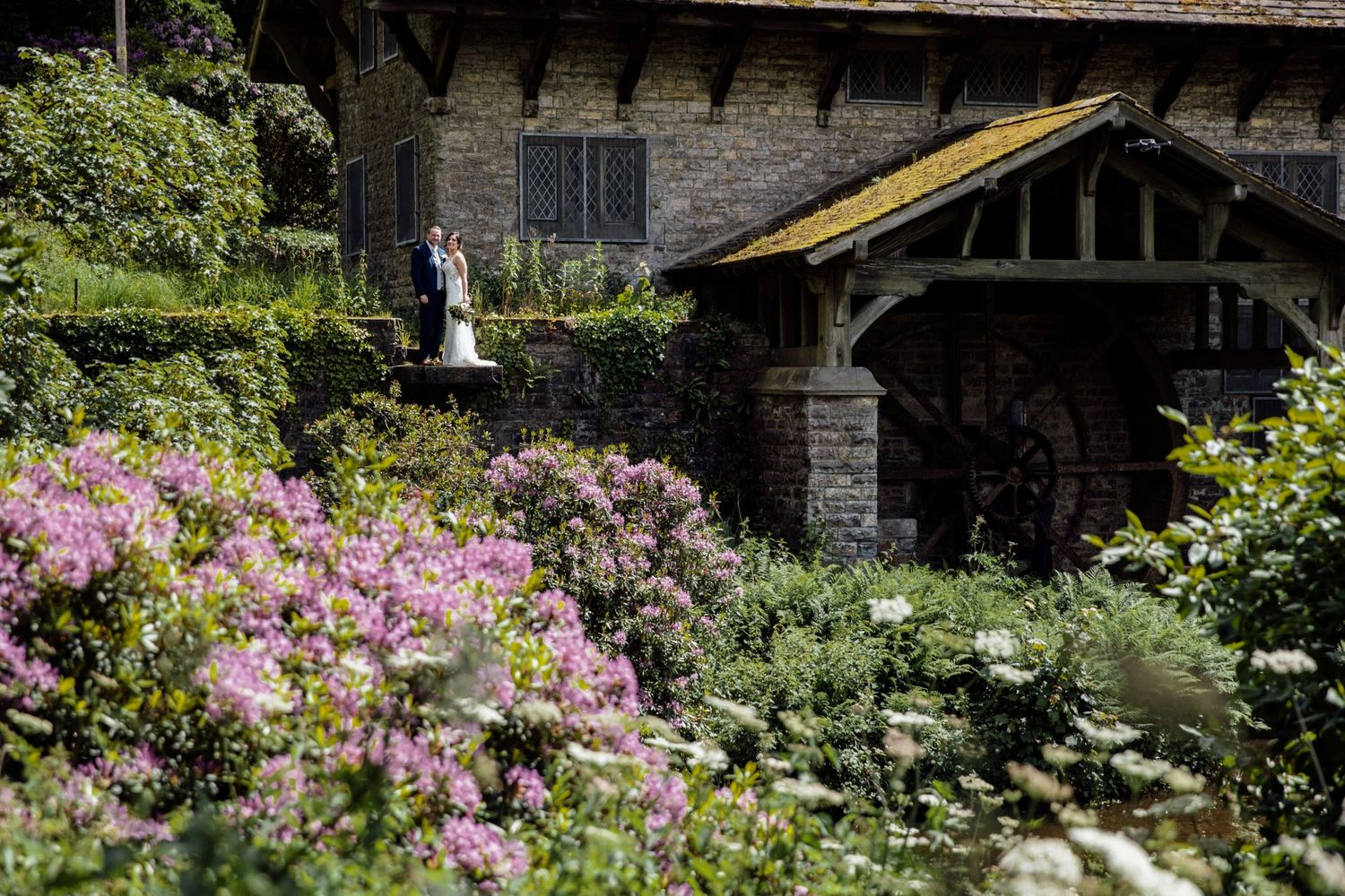 Stone building exterior with blooming pink flowers and garden landscaping.