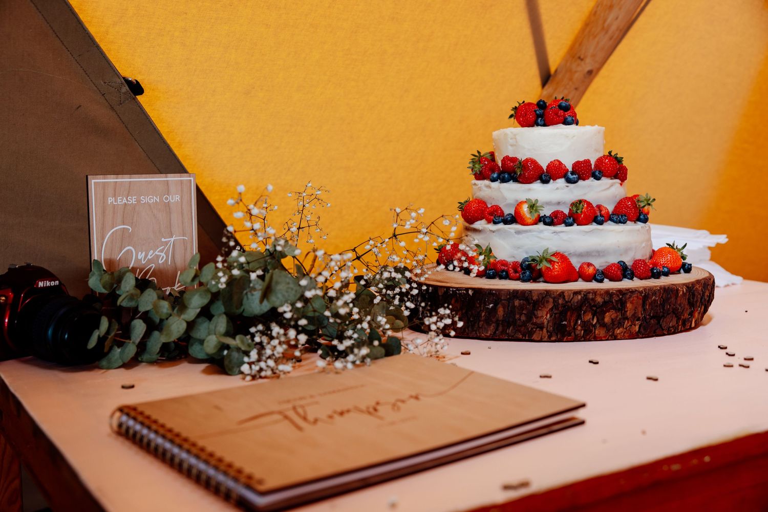 Rustic wedding cake display with strawberry decorations and wooden elements on orange background.