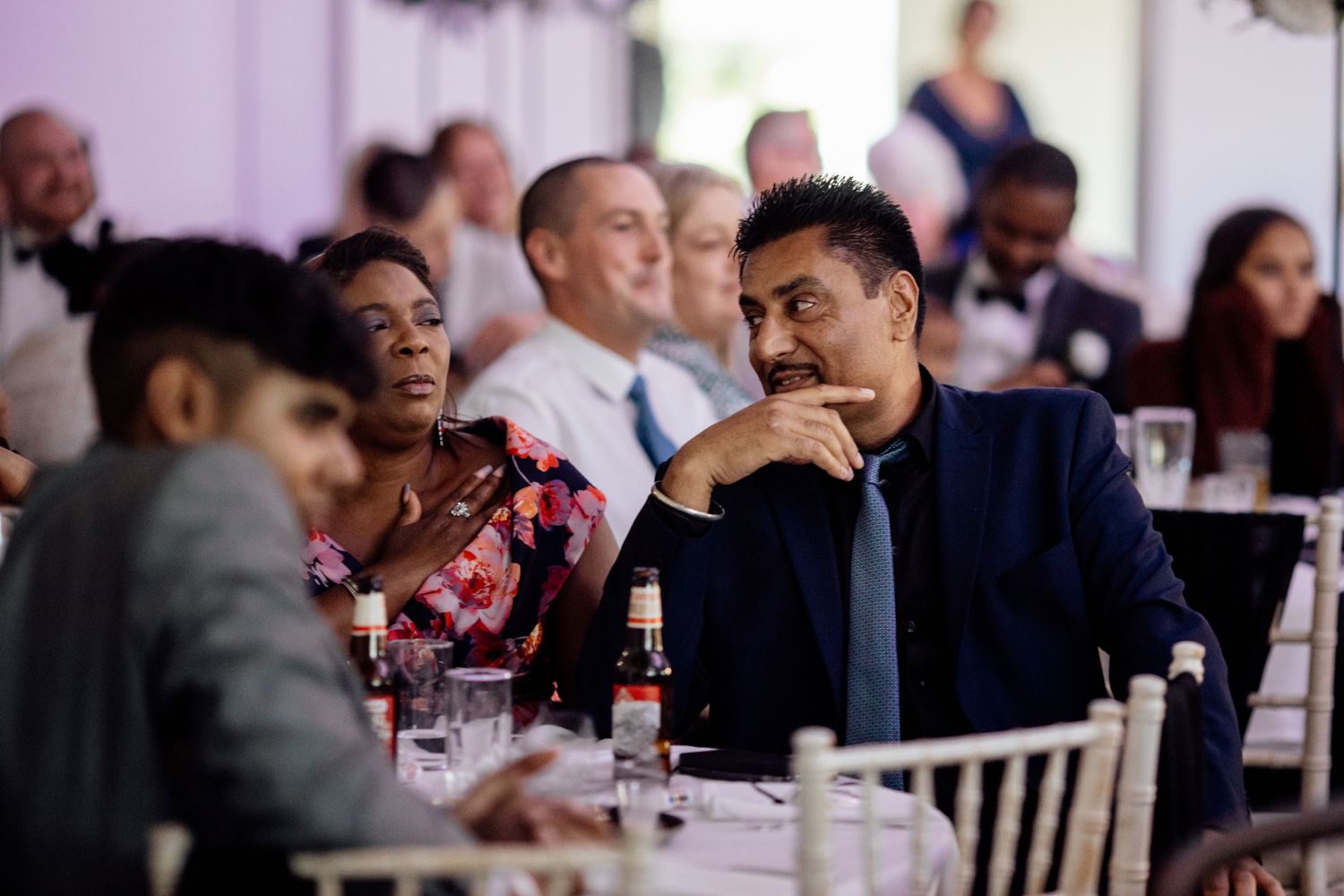 Wedding reception guests enjoying conversation at tables during dinner service.