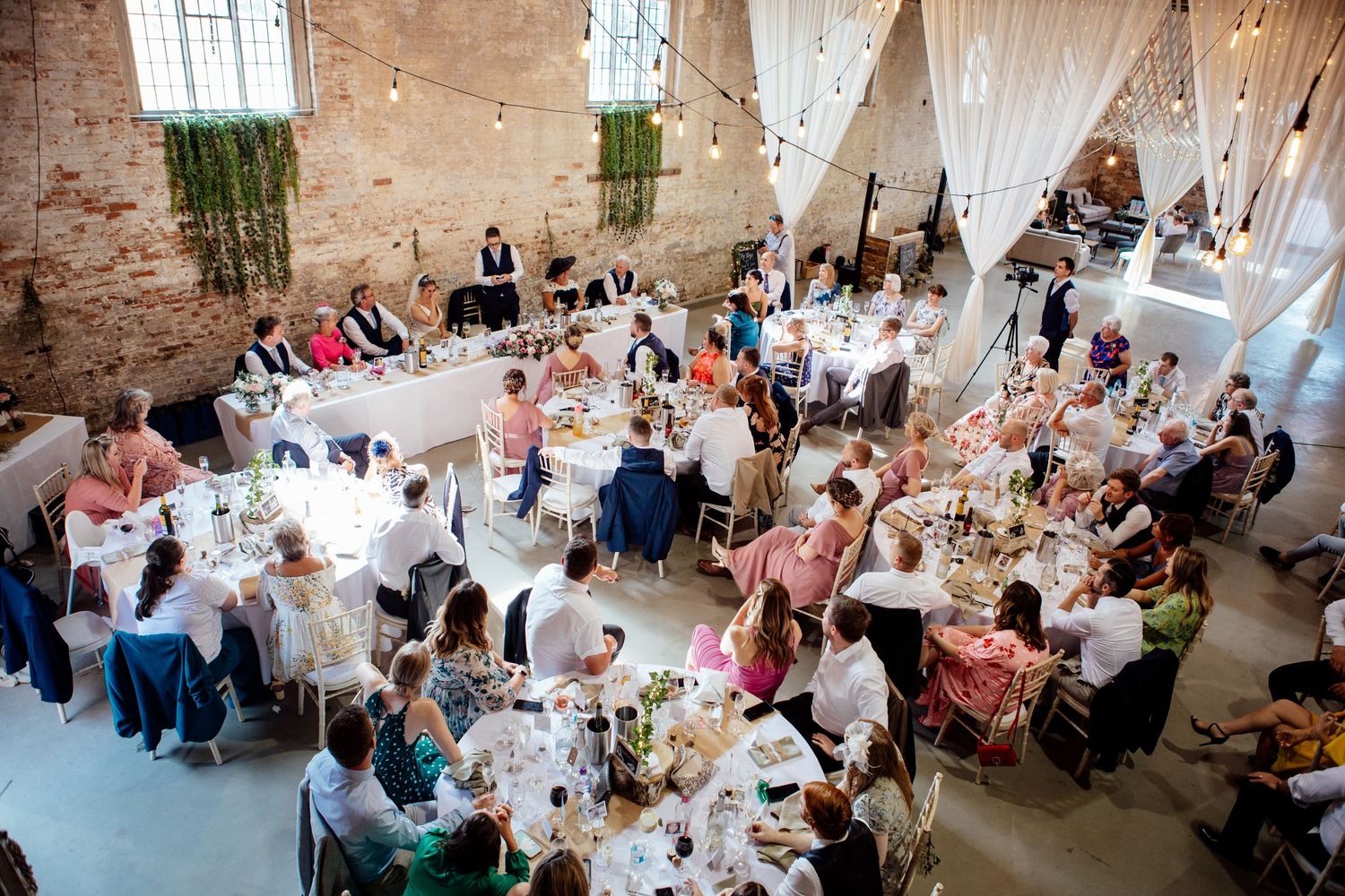 Wedding reception setup in a rustic brick venue with elegant table settings and white draping.