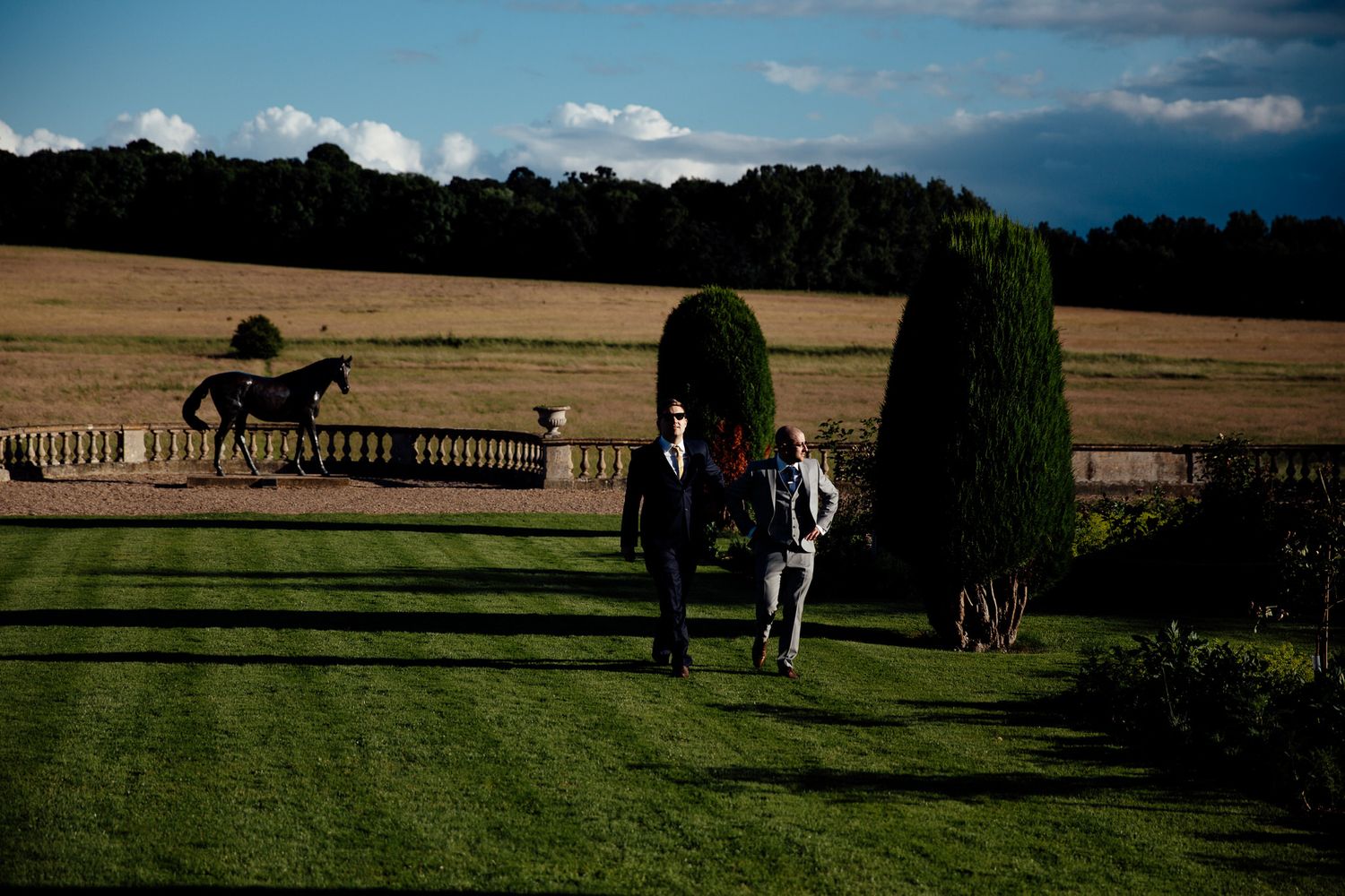 Wedding party explores scenic countryside estate grounds on sunny afternoon.
