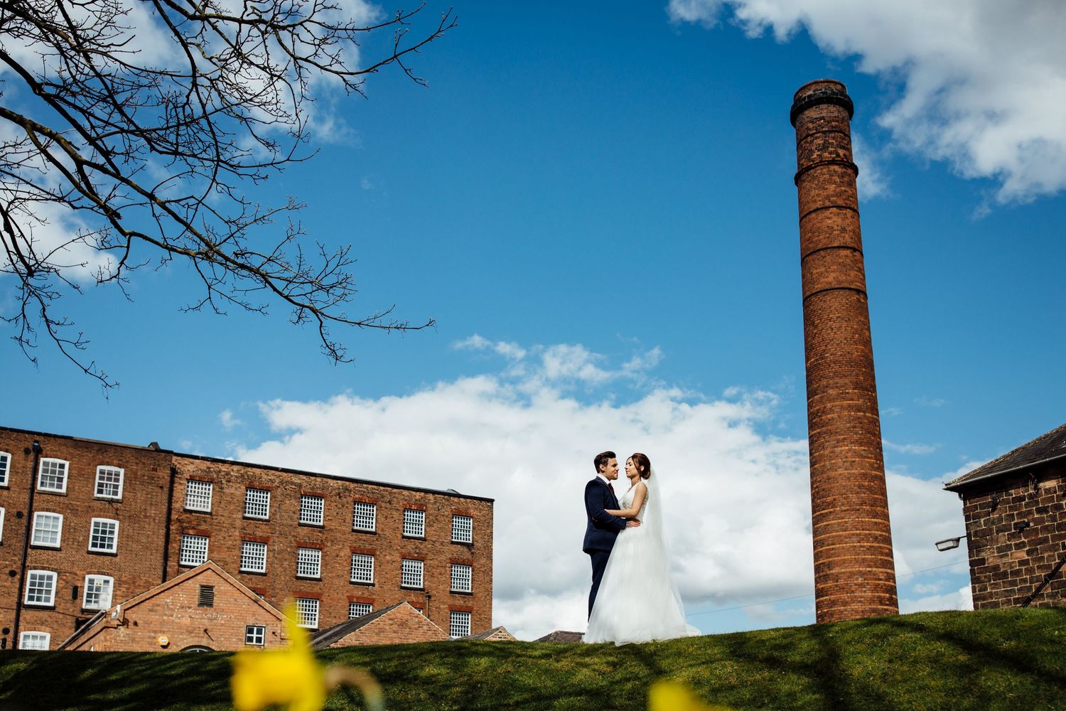 Wedding couple photographed against industrial backdrop with brick buildings and chimneys.
