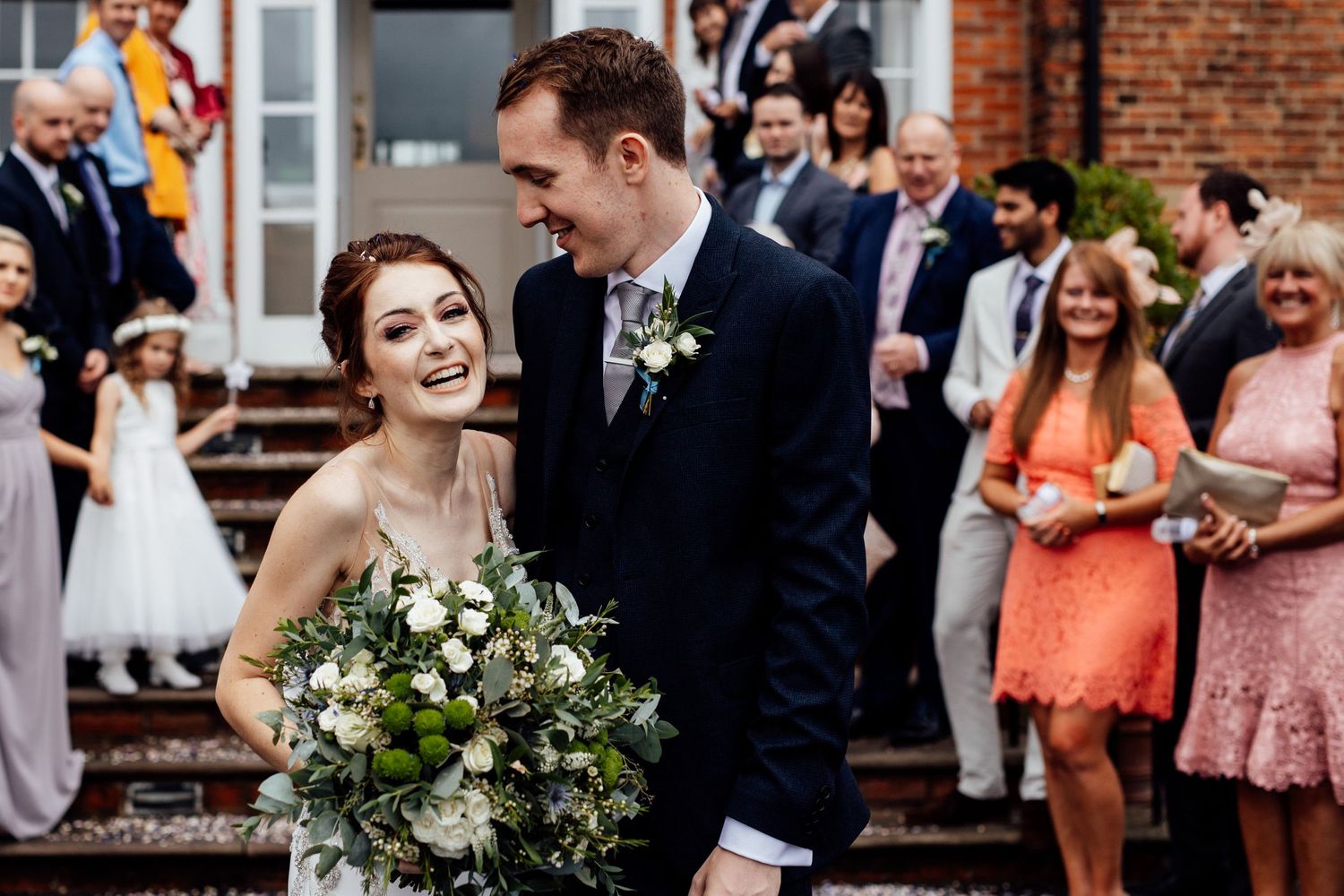 Wedding celebration outside a historic brick building with guests gathered around a happy couple.