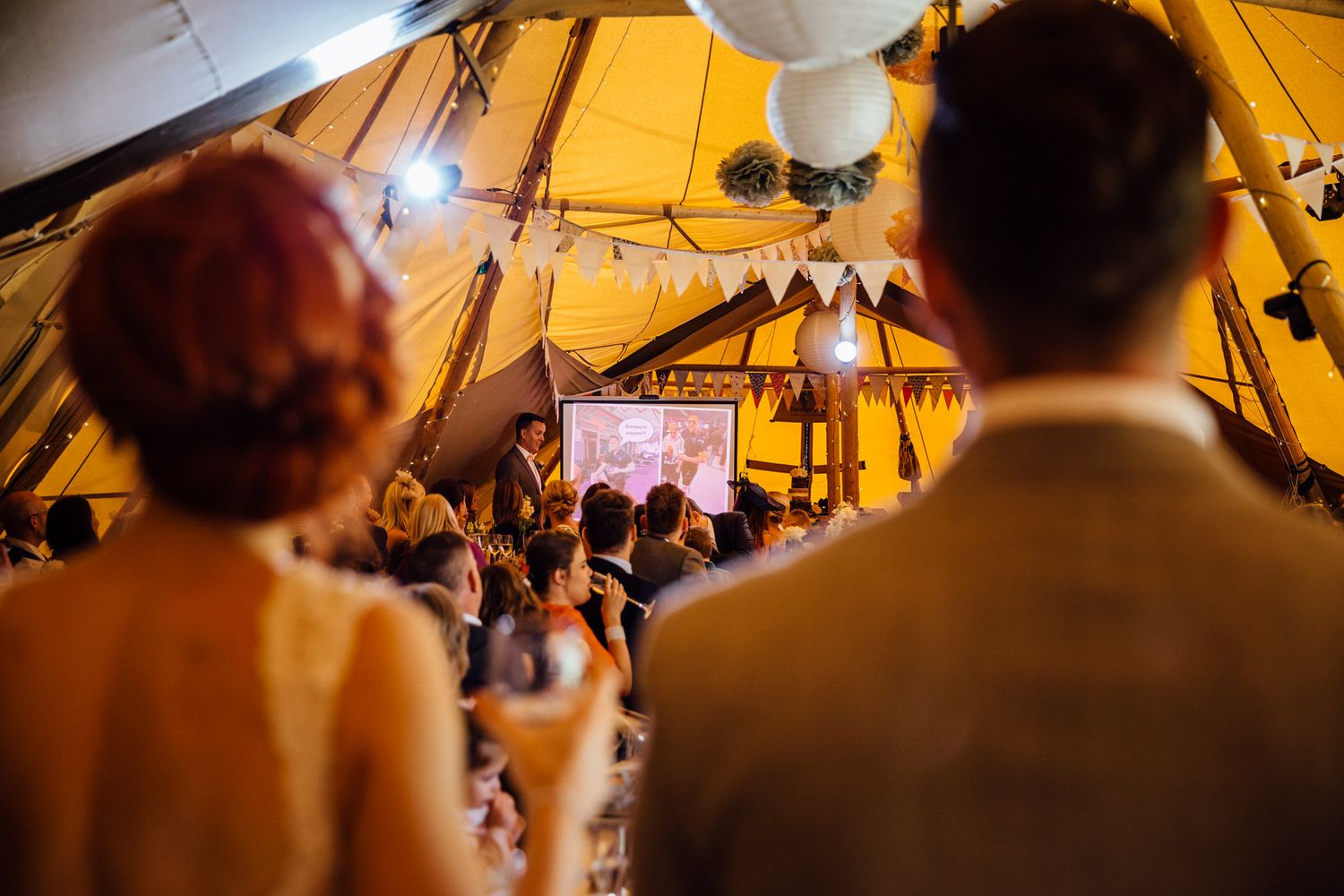 Evening wedding celebration under a tipi tent with ambient lighting and festive decorations.