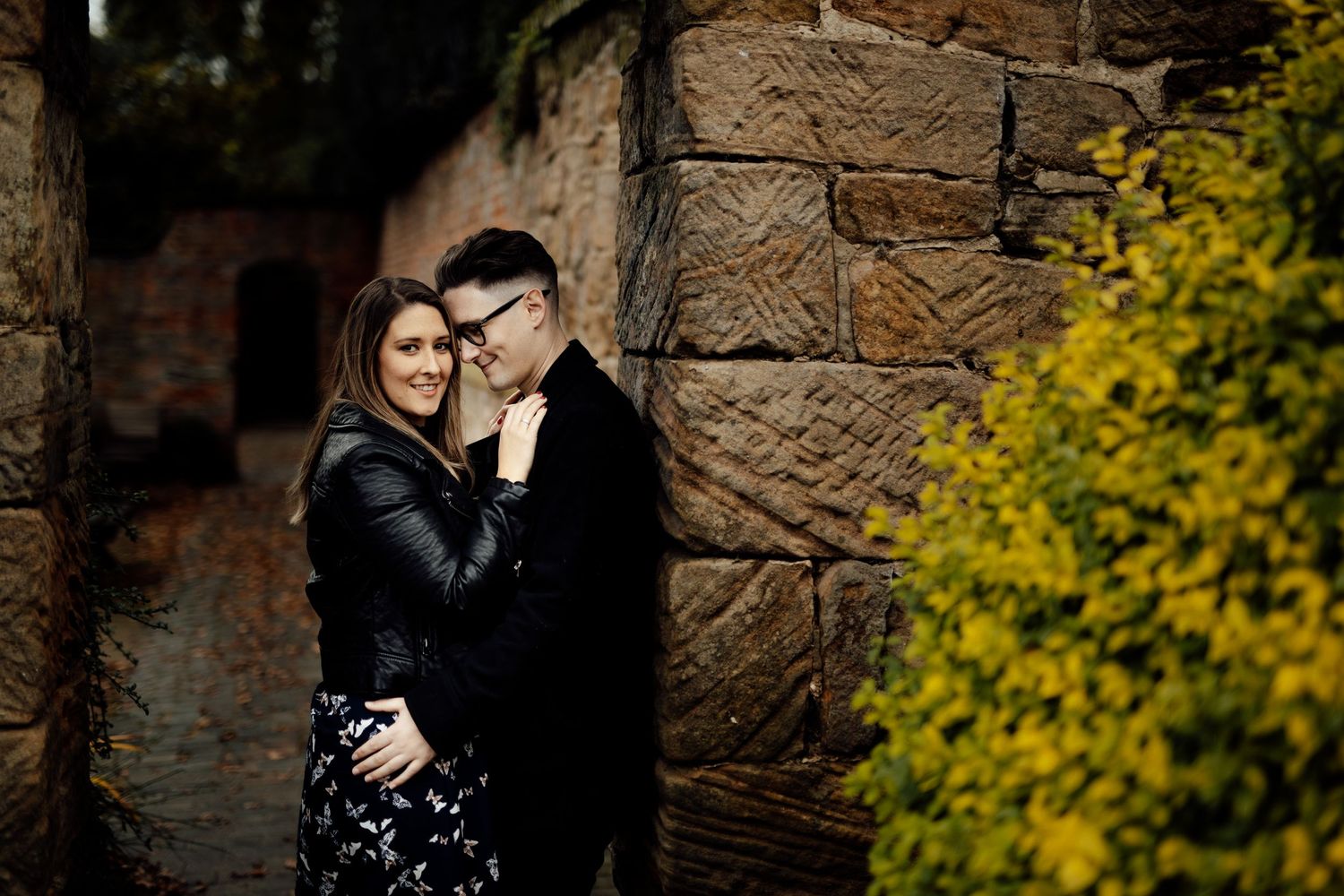 Couple sharing tender moment near historic building with autumn foliage.