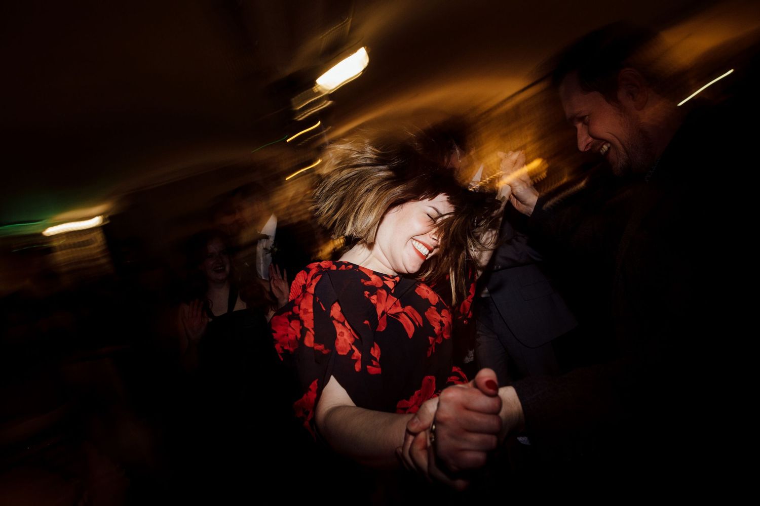Couple dancing energetically at a dimly lit party with motion blur and ambient lighting effects.