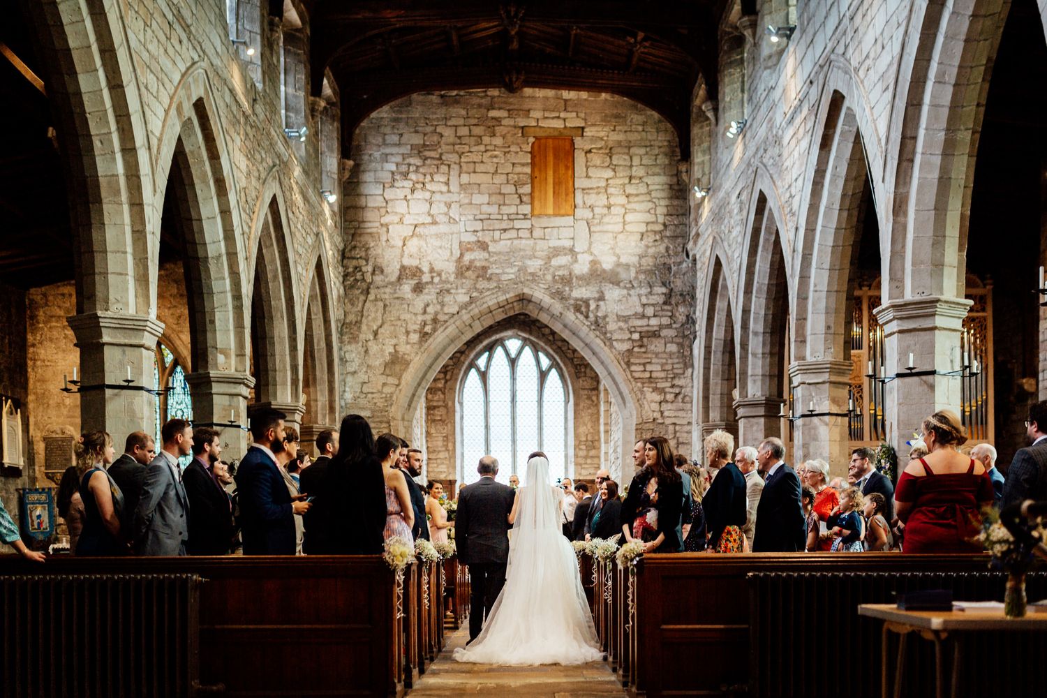 Panoramic view of a wedding ceremony in a historic stone church with vaulted ceilings and arches.