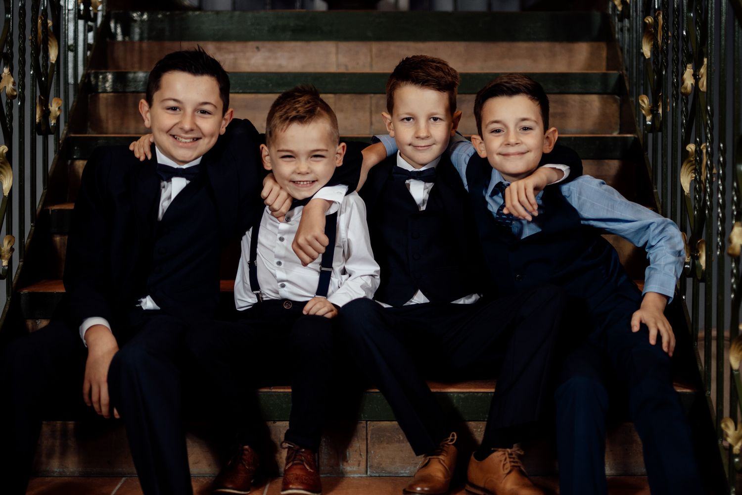 Group photo of young boys in formal attire sitting on dark leather furniture.
