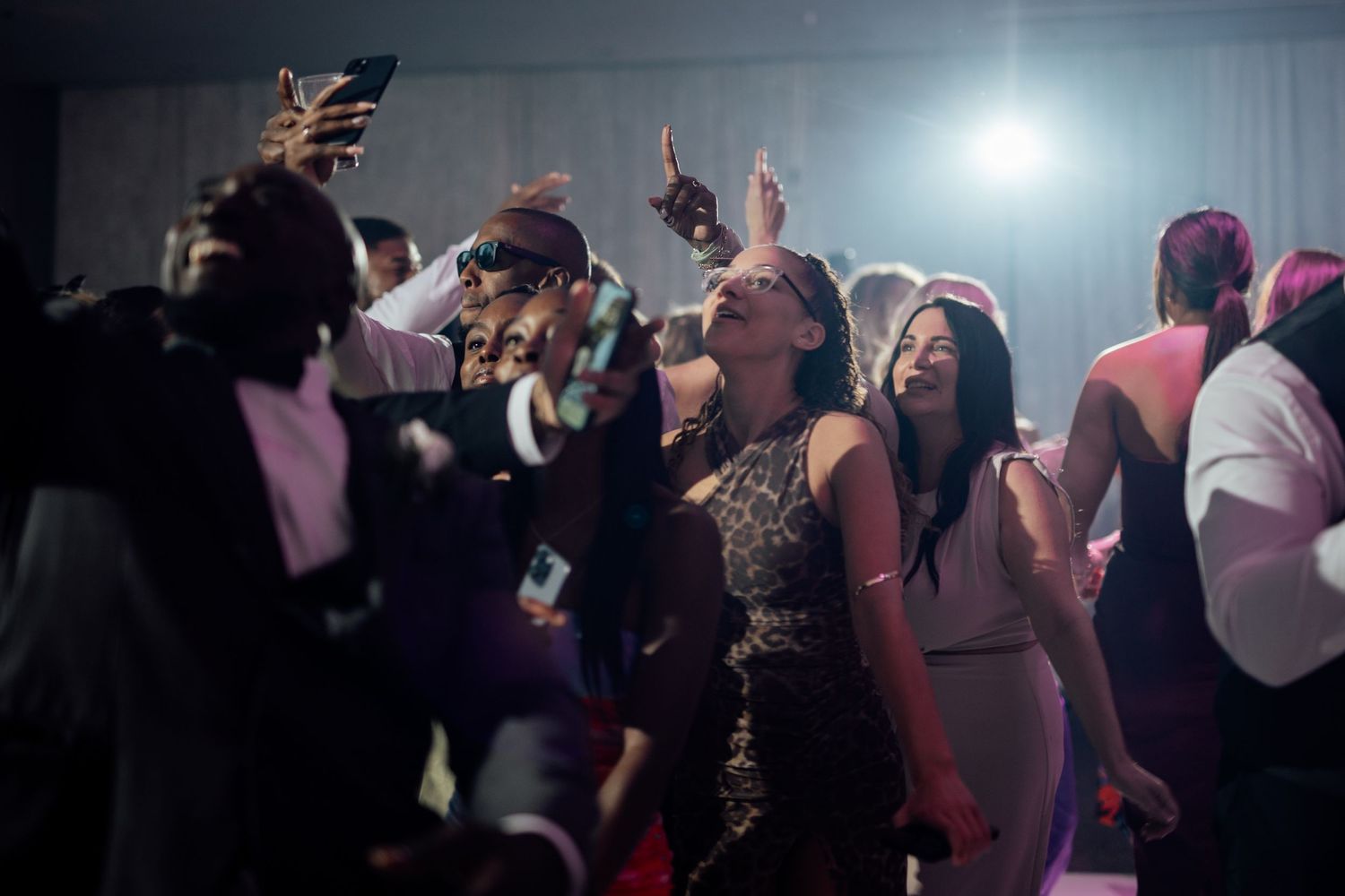 Energetic wedding reception dance floor scene with guests celebrating under party lights.