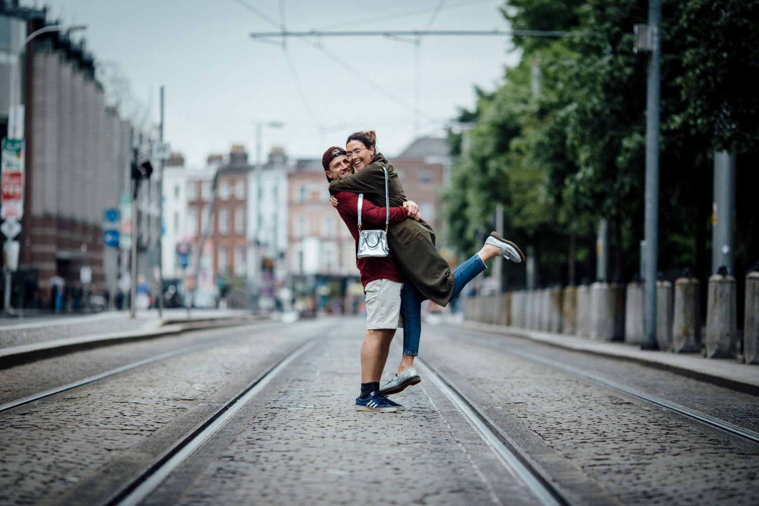 Couple embracing on train tracks in middle of city street.