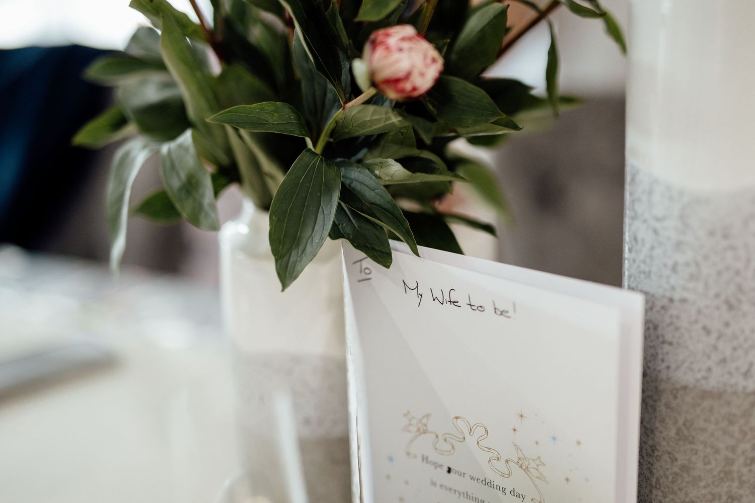 White ceramic vases with delicate floral arrangements line a wedding reception table.
