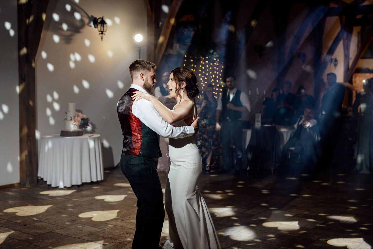 Newlyweds share their first dance under spotlights creating magical patterns on the dance floor.