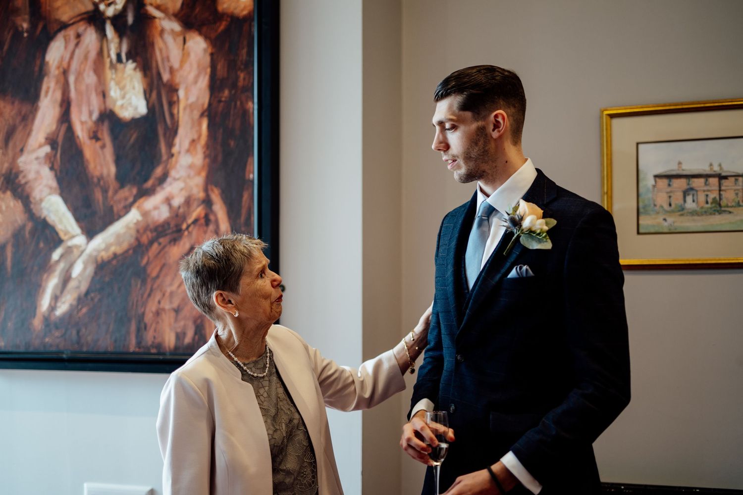 Intimate moment between groom in navy suit and older relative in formal attire.