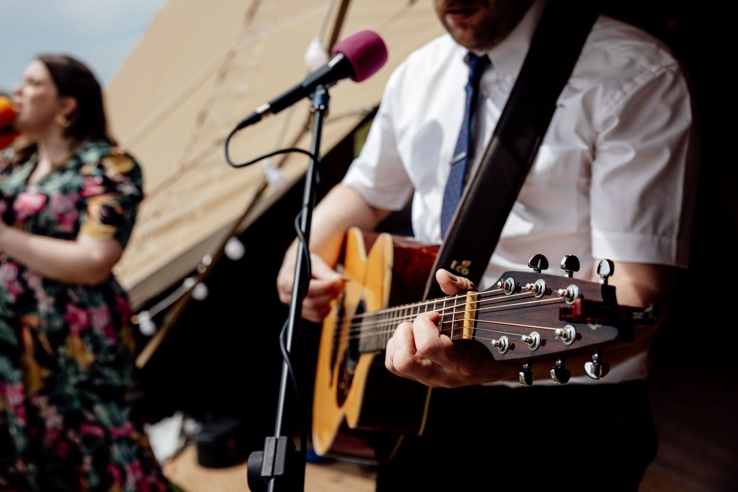 Musician playing acoustic guitar at outdoor wedding reception with microphone setup.