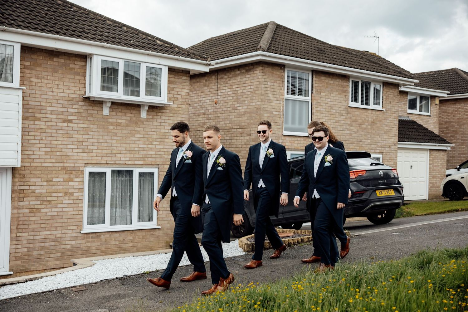 Groomsmen walking together down a residential street in matching dark suits.