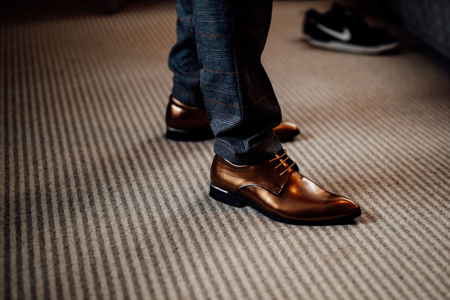 Detail shot of dress shoes and formal wear on textured carpet.