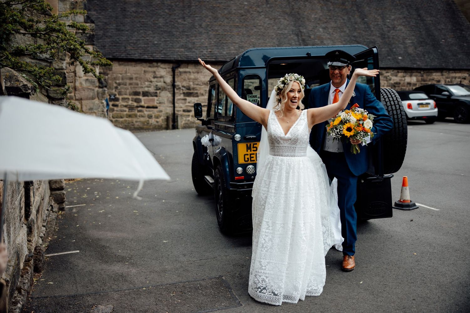 Wedding celebration outside stone building with vintage car in background.