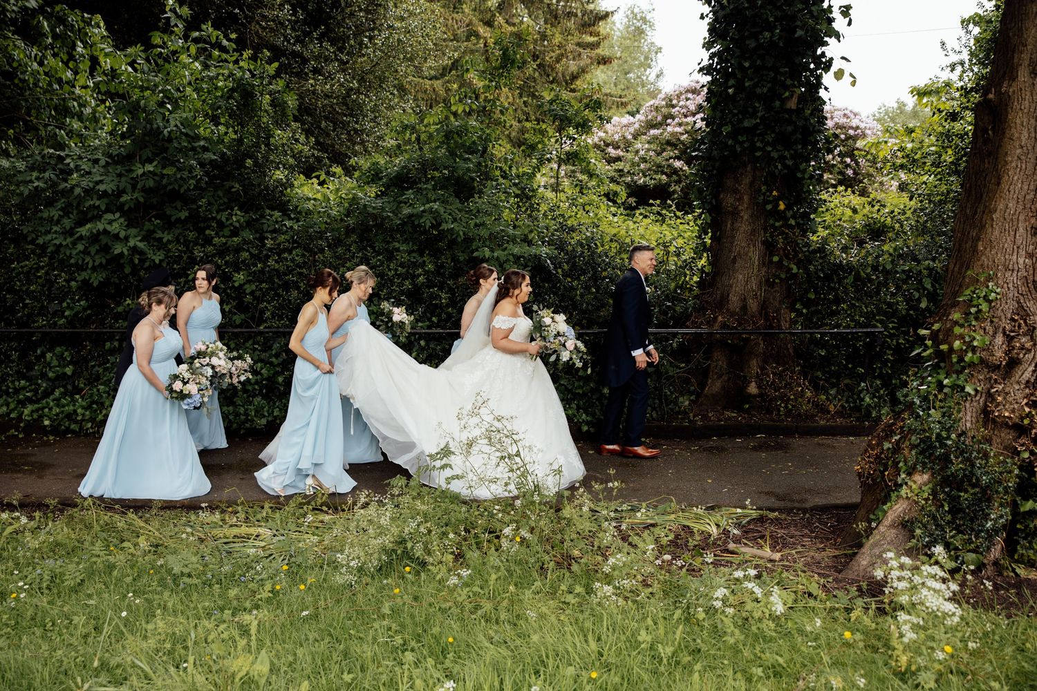 Wedding party relaxing on grass in a garden setting with trees in background.