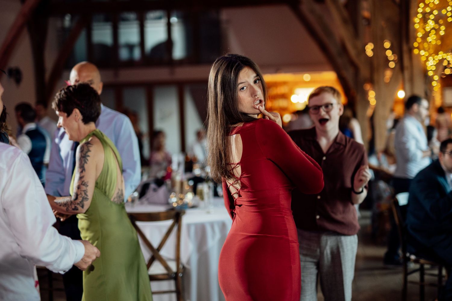 Wedding reception dance party with guests celebrating under warm string lights in a rustic venue.