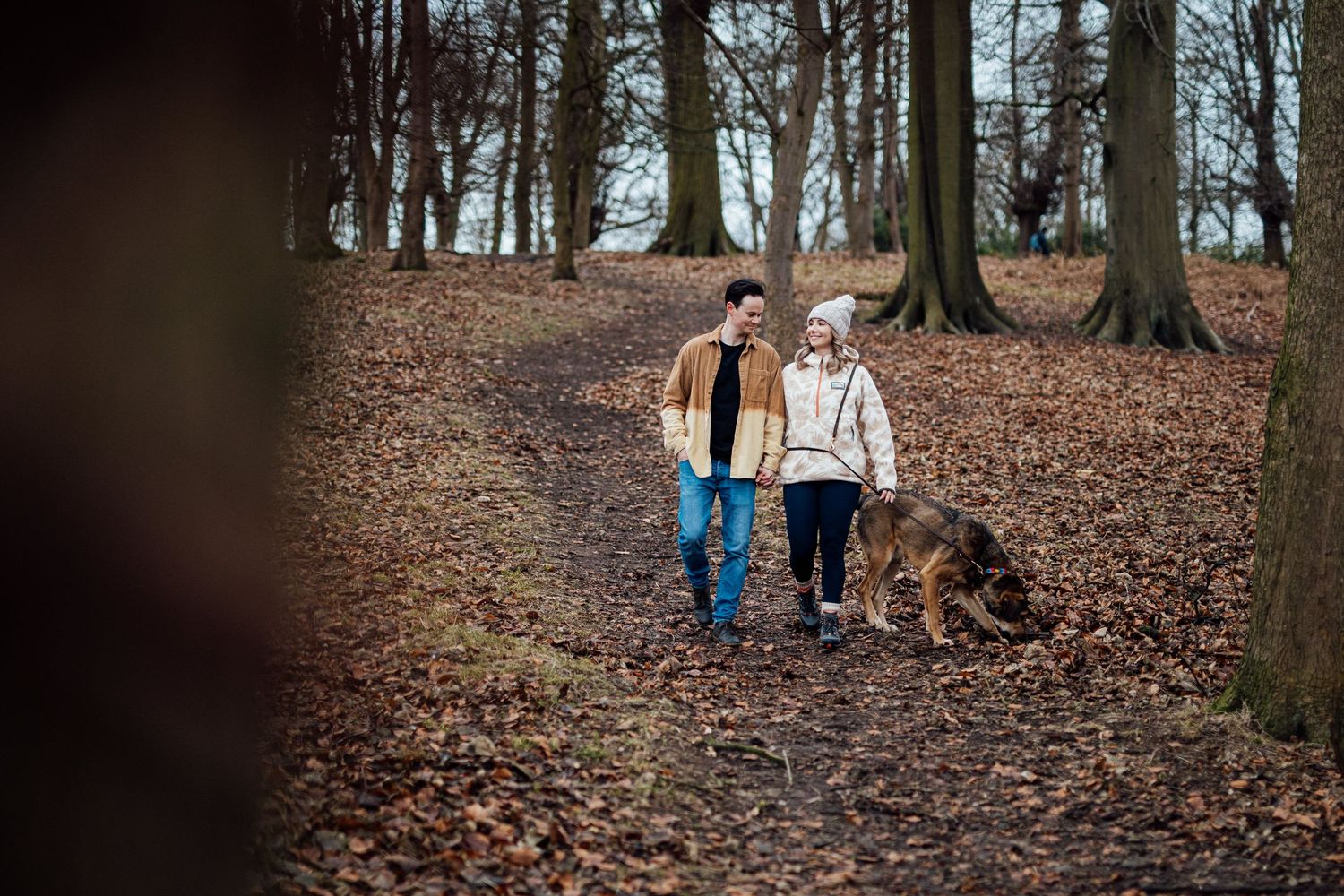 A couple walking together on a leaf-covered path through an autumn forest.