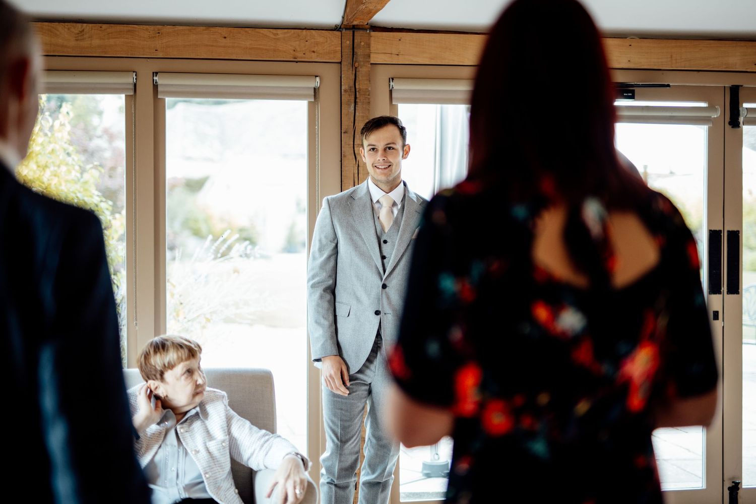 Wedding party members in formal attire gather inside a bright sunlit room.