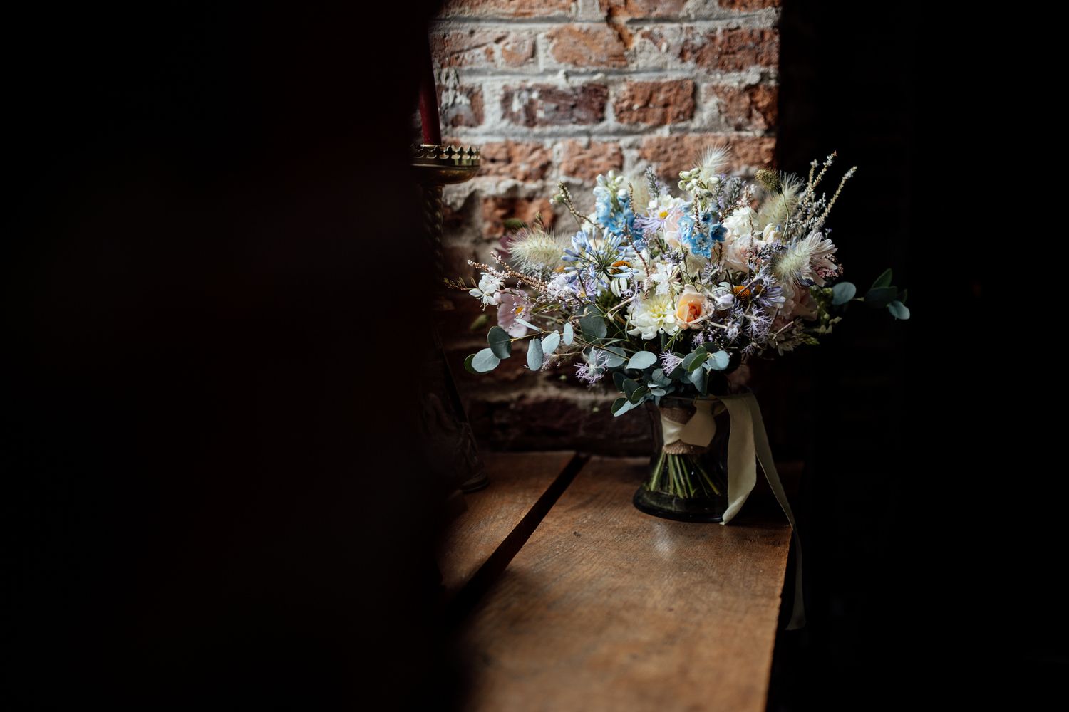Wedding floral arrangements against exposed brick wall in moody lighting.