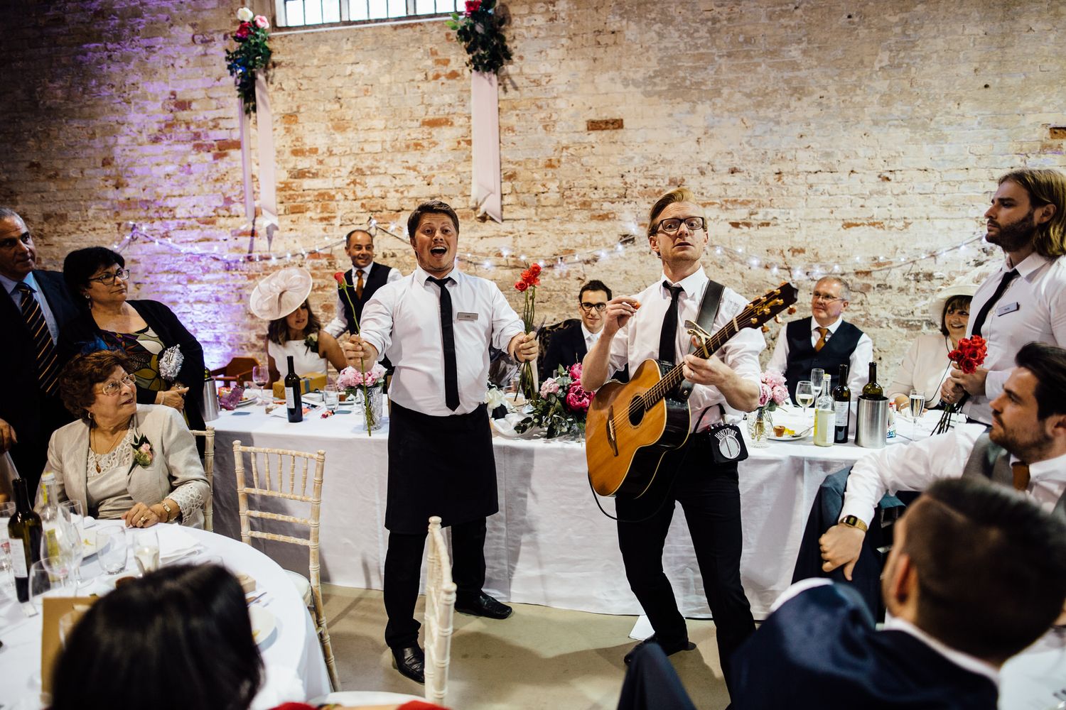 Wedding entertainment performers playing music in front of exposed brick walls with purple lighting.
