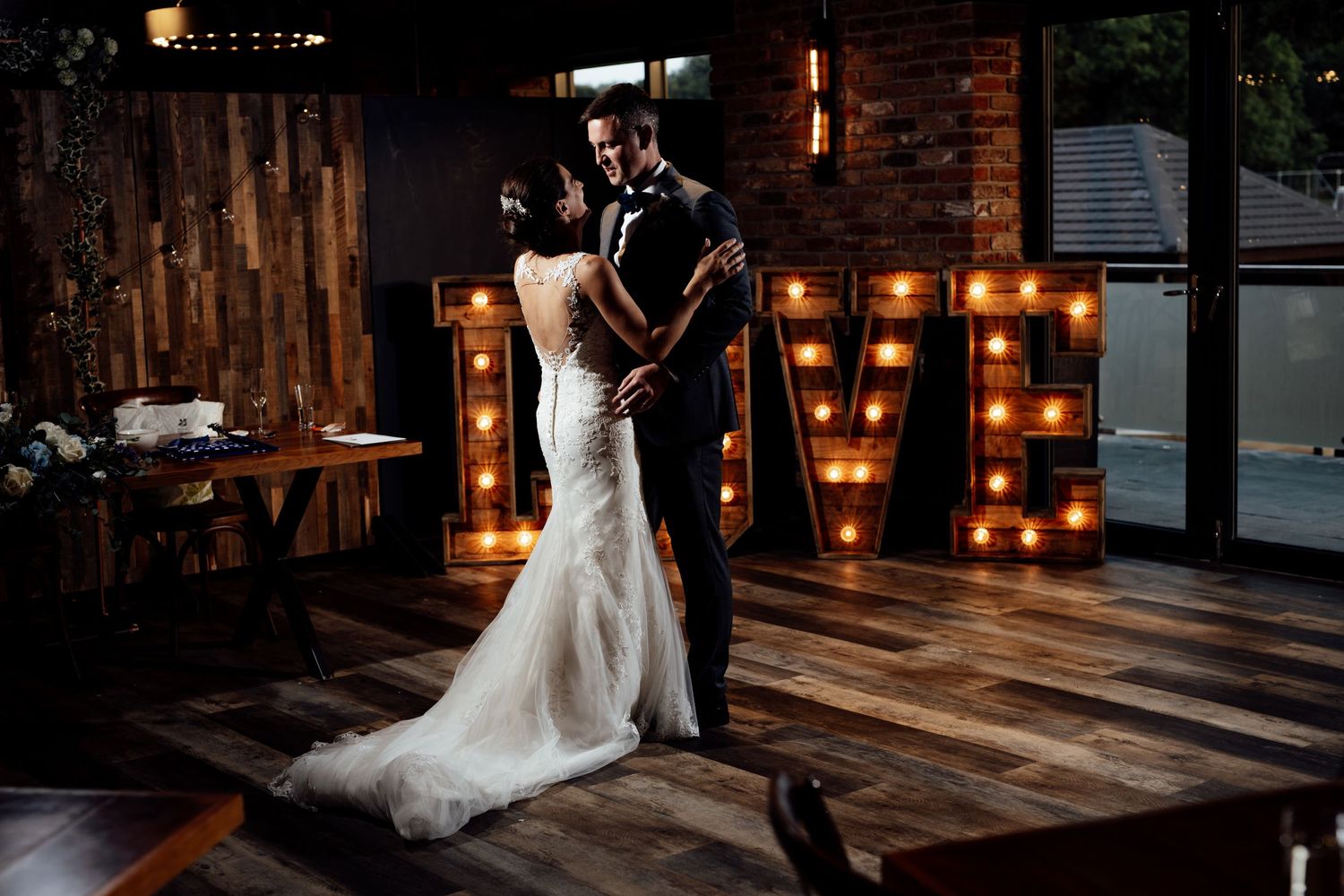 Wedding reception venue with rustic wooden floors and warm glowing marquee lights.
