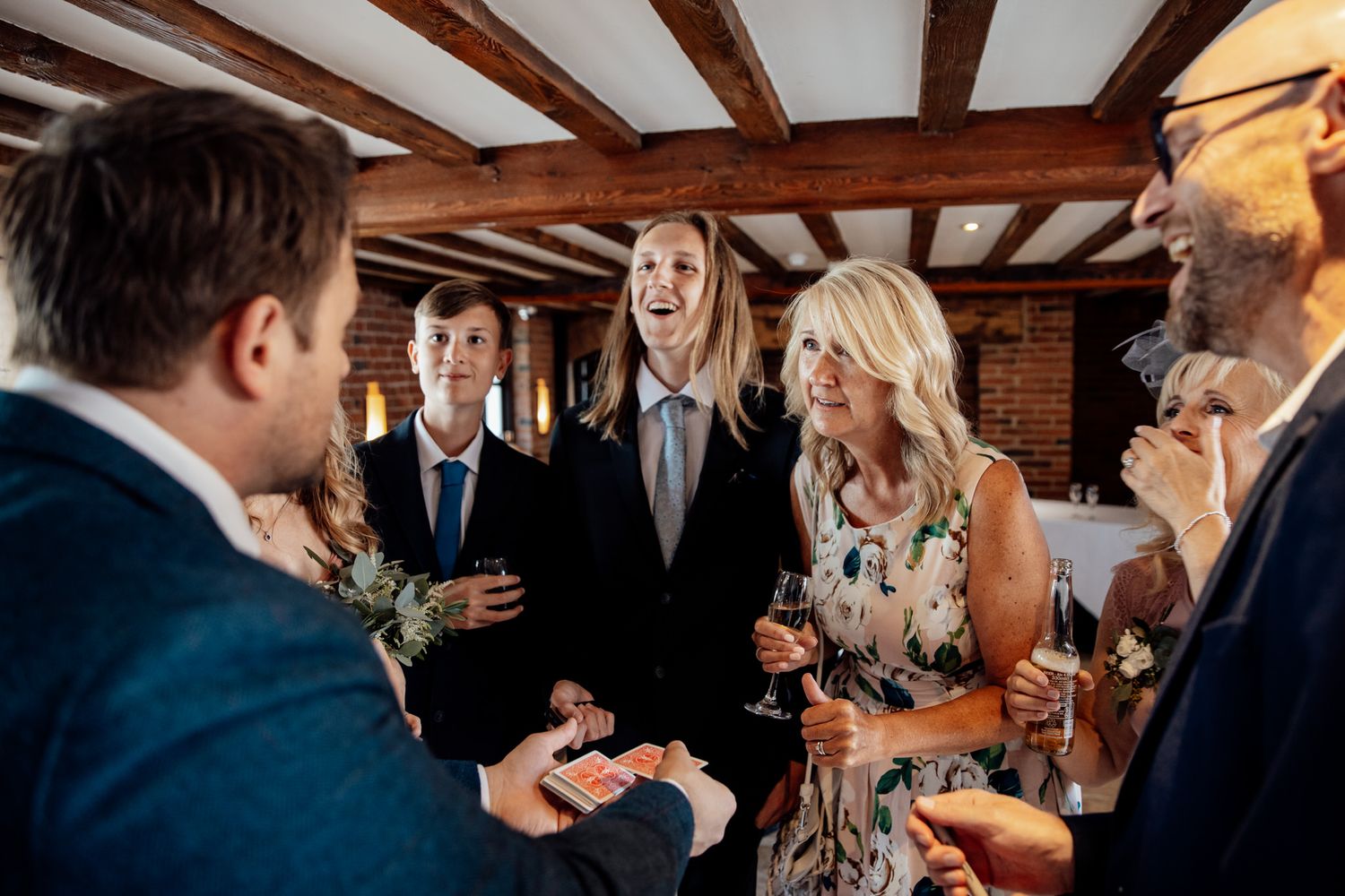 Wedding reception gathering in rustic venue with exposed wooden ceiling beams.