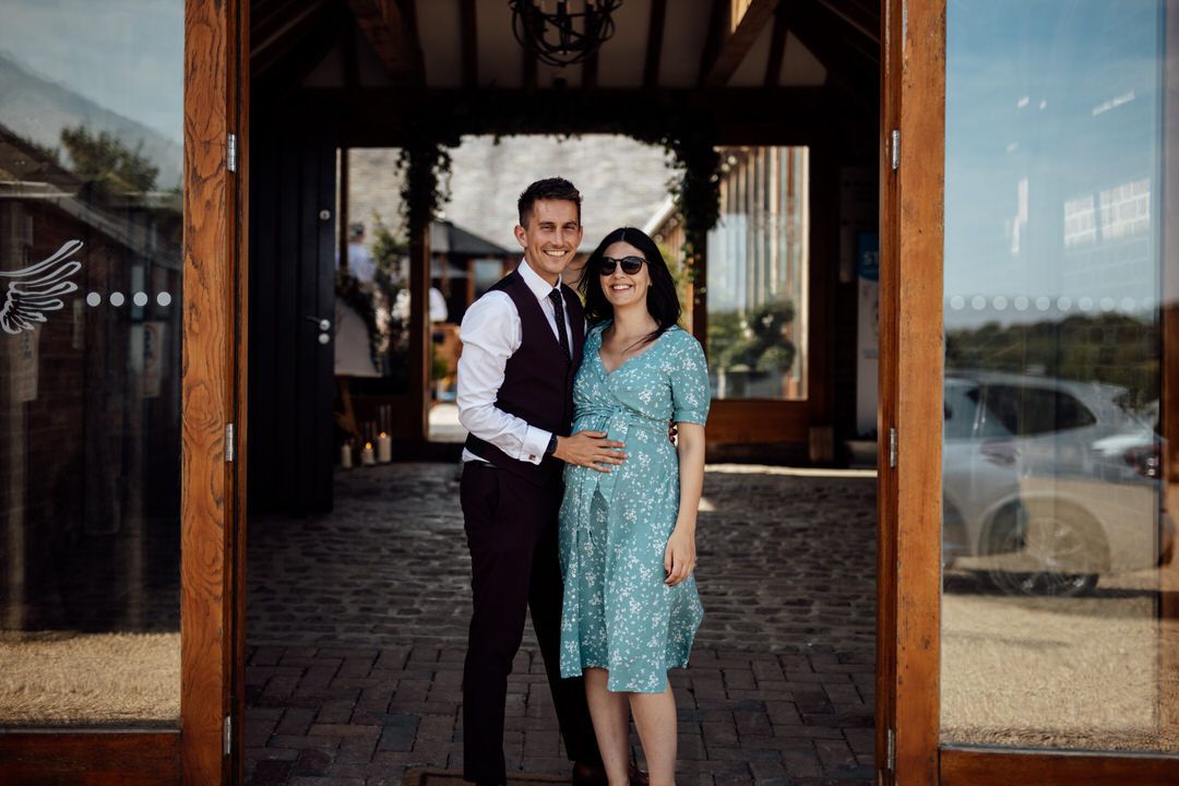 Couple poses outside rustic wooden building at sunset during wedding celebration.