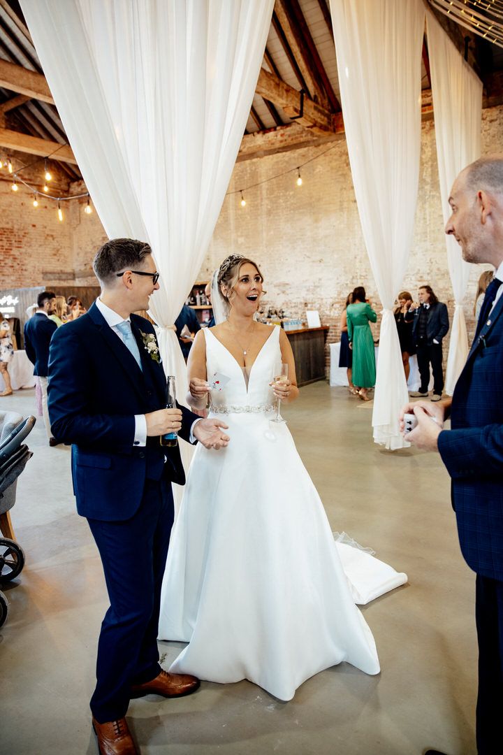 Wedding reception guests dancing and celebrating in a rustic barn venue with white drapes and exposed beams.