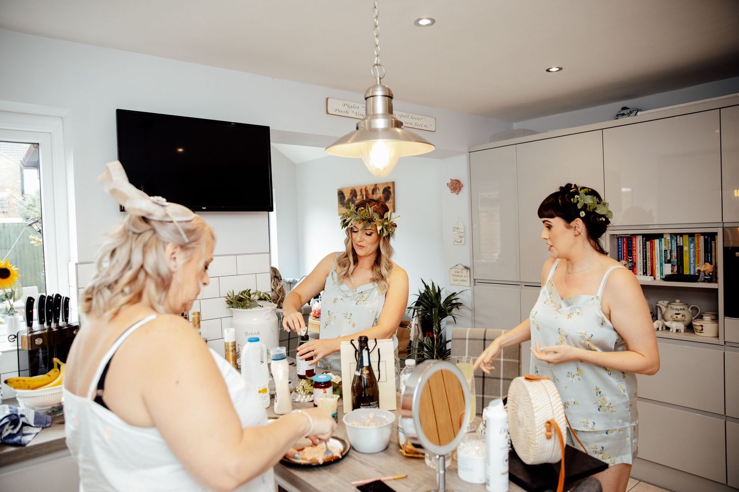 Wedding party getting ready in a bright modern kitchen with makeup and hair styling preparations.